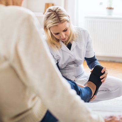 Pflegedienst hilft pflegebedürftiger Frau beim Anziehen der Schuhe 